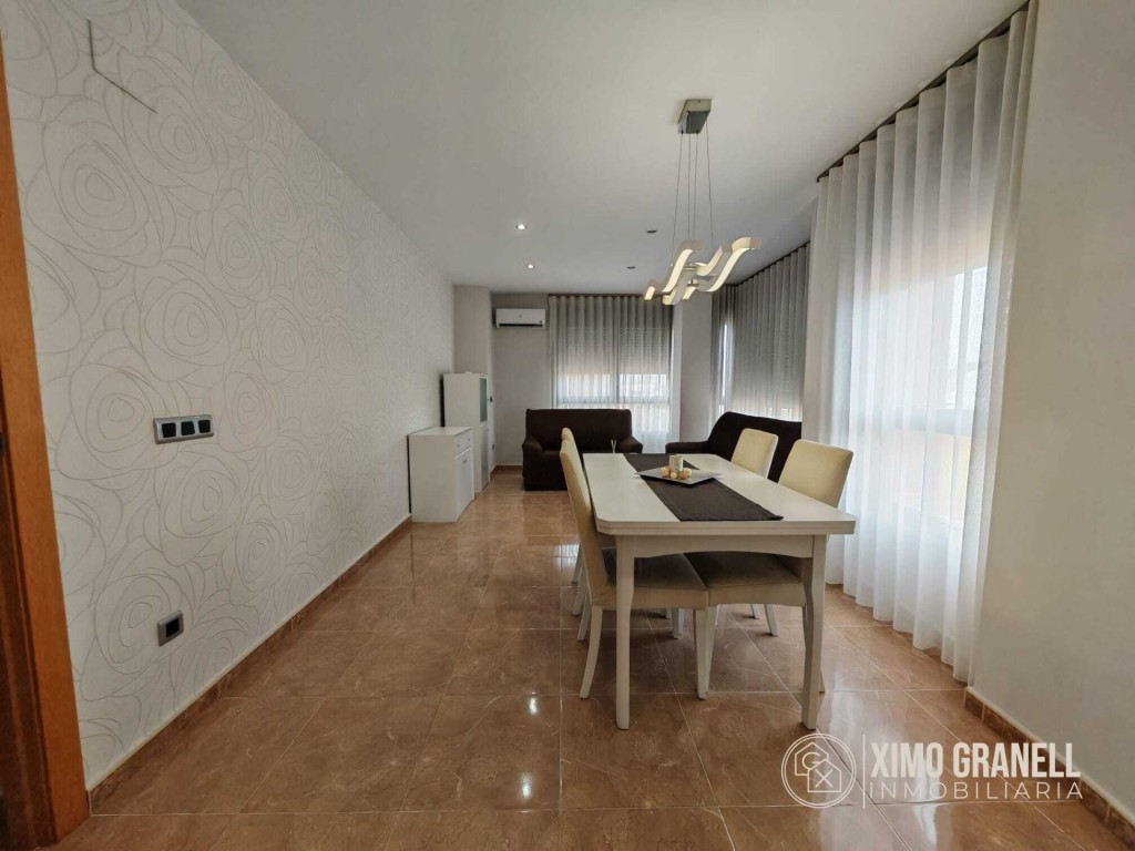 Comedor y salón luminosos con mesa para seis, sofá y grandes ventanales con cortinas