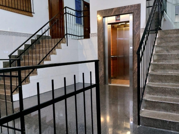 Interior building lobby showing two staircases on either side and a central elevator with a marble-framed doorway; polished floor and white walls.