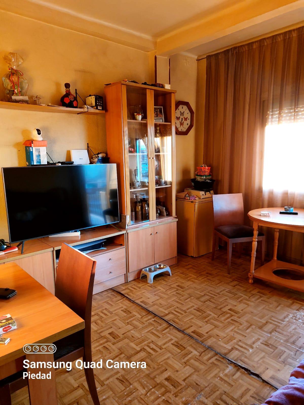 Flat-screen TV on a wooden cabinet with a glass-front display cabinet nearby, round dining table, and brown curtains in a warm living room.