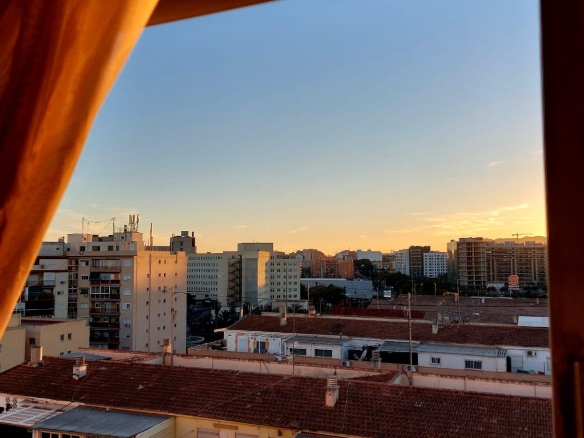 Sunset over a city skyline viewed from a window, with a brown curtain on the left side.